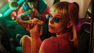 κοπέλα τρώει ένα κομμάτι πίτσα μέσα σε αυτοκίνητο