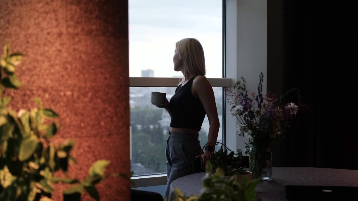 γυναίκα με καφέ κοιτάζει έξω από το παράθυρο