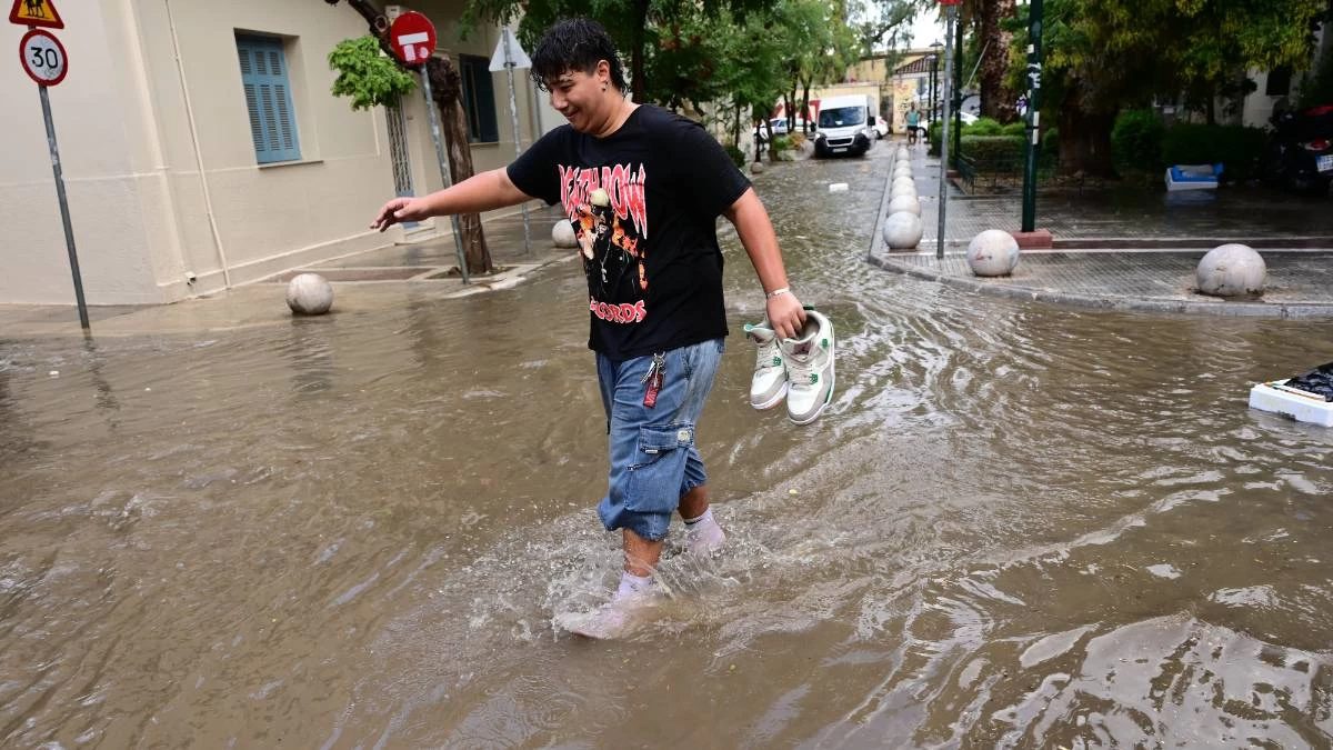 Άνθρωπος με παπούτσια στο χέρι περπατάει μέσα σε πλημμυρισμένους δρόμους