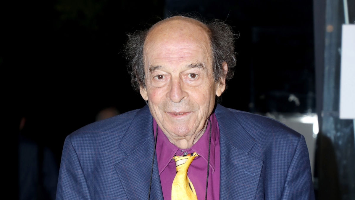 Ο Μανούσος Μανουσάκης με μωβ πουκάμισο, κίτρινη γραβάτα και μπλε σακάκη