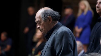 Ο Μανούσος Μανουσάκης με γκρι σακάκι και σκυμμένο κεφάλι