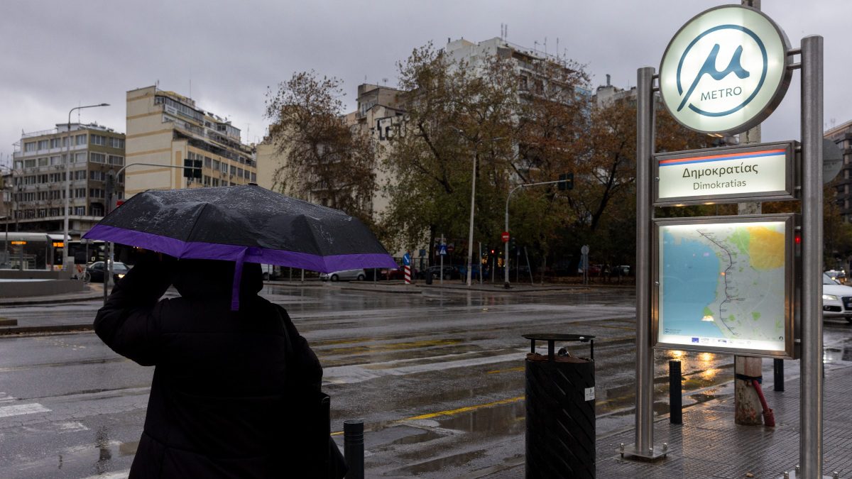 Βροχερή μέρα και μία κυρία με ομπρέλα δίπλα σε σταθμό μετρό