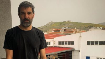 Ο Πέτρος Λαγούτης με φόντο σπίτια και λόφο