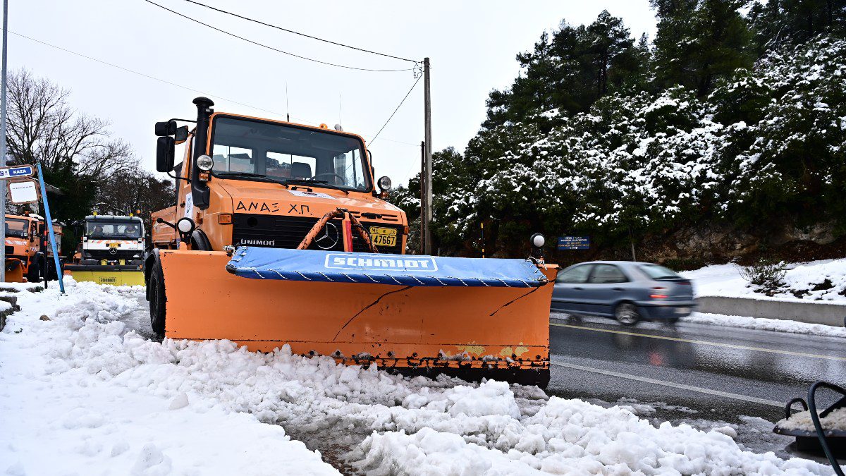 Χιονισμένος δρόμος και ένα πορτοκαλί εκχιονιστικό